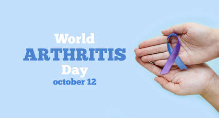 World Autoimmune Arthritis Day. Adult hands holding blue purple ribbon on blue background. RA rheumatoid arthritis illness disease.の写真素材