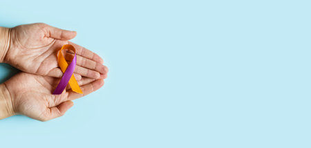 World Psoriasis Day. Woman's hands are holding a purple-orange ribbon on a blue background. Treatment of skin diseases, dermatitis, eczema, psoriasis. medical banner. copy spaceの写真素材