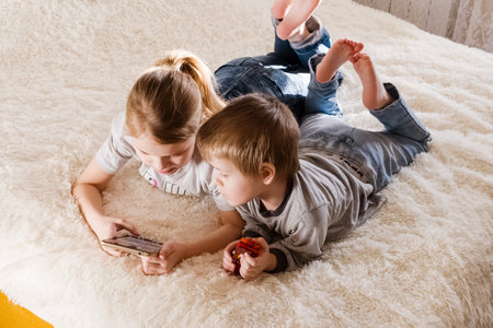 Children are lying on the bed, watching cartoons, playing a game on a smartphone 12.01.23 .Tula, Russiaの写真素材