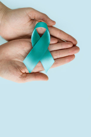 Hands of woman holding Teal ribbon on blue background, Symbolic for cervical cancer, ovarian cancer, gynecological cancer and PCOS. And sexual assault awareness.の写真素材