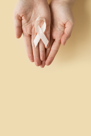 Womans hands hold Peach Ribbon on beige background. Uterine Cancer Awareness month. Healthcare and...