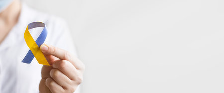 World down syndrome day. A female doctor in a white coat holds blue and yellow ribbon. Down syndrome awareness concept. top view. copyspace. bannerの写真素材