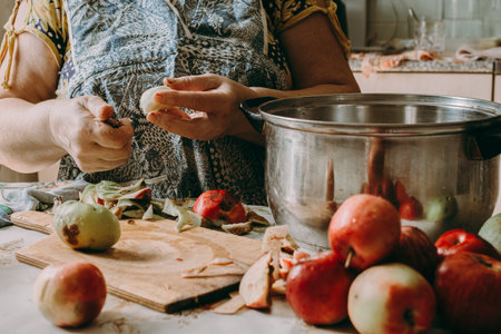 Old woman cuts apples for jam. Red ripe apples on the table next to the jam pot. An elderly woman makes jam in her cottage on a farm. Conservation and harvesting. Homemade delicious foodの写真素材