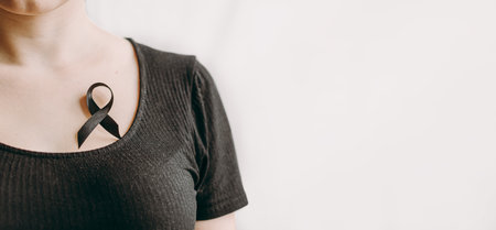 The woman's hand holds black Ribbon for symbol Melanoma and skin cancer. medical banner with copy spaceの写真素材