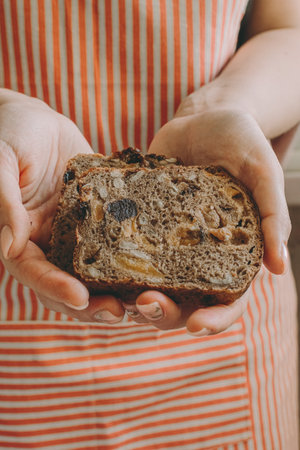 A woman holds in her hands healthy vegetarian gluten-free bread with cereals, prunes, dried...