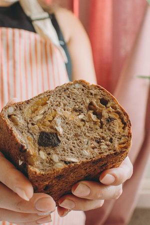 A woman holds in her hands healthy vegetarian gluten-free bread with cereals, prunes, dried...