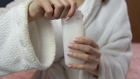 Woman closes the lid of shampoo. Woman in a bathrobe holds a jar of travel shampoo. Close-upの写真素材