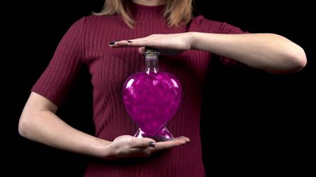 Young woman holds a bottle with a love potion. Glass bottle in the form of a heart with pink liquid. Valentines Day is the day of all lovers.の写真素材
