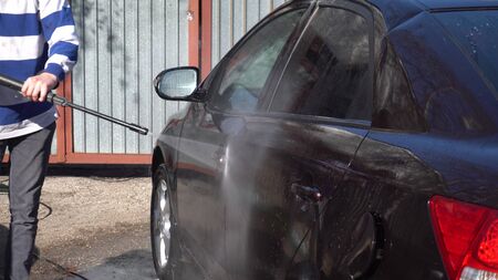 A man washes dirt off a car with a high-pressure water jet. Special detergent for car wash. Washes a car in front of the house.の写真素材