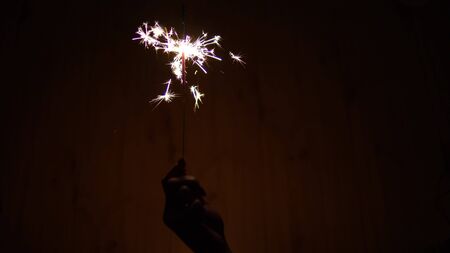A woman holds a Bengal fire in her hand. Sparklers shine in the dark. Hand with a sparkler closeupの写真素材