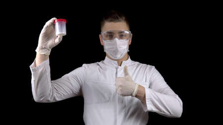 Young man doctor checks sperm tests. A man examines a test jar, then shows a thumb up. Positive semen analysis. On a black background.の写真素材