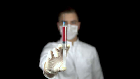 Blood in a syringe close-up on a black background. A man doctor holds out a syringe with blood to the camera.の写真素材