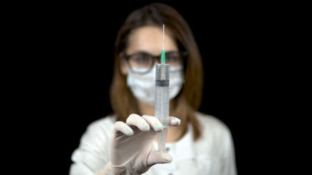 Woman doctor holds out a syringe to the camera. Syringe with the drug close-up. A doctor sprays from a syringe to release air on a black background.の写真素材