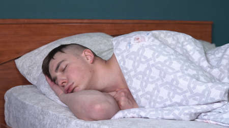 A young man is sleeping with a funny expression on his face. A man lies in bed in his room.の写真素材
