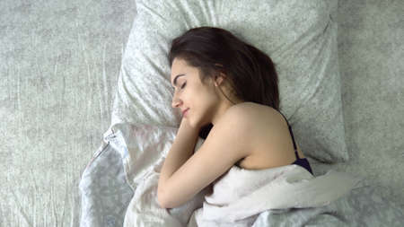A young woman is sleeping under the covers. A girl lies in bed in his room. View from above.