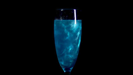 Glass with blue liquid. The elixir spins and overflows with liquid. Potion of love is isolated on a black background.の写真素材