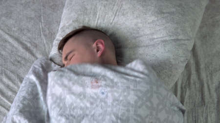 A young man cannot fall asleep. A man lies in bed in his room and suffers from insomnia. View from...