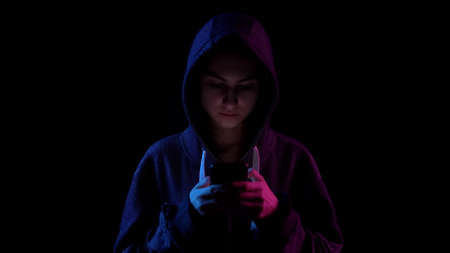 A young woman in a hood with a phone in her hands. Hacker makes a hack through the phone. Blue and...