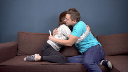 A young woman shows a positive pregnancy test to a young husband. A man rejoices and hugs his wife....