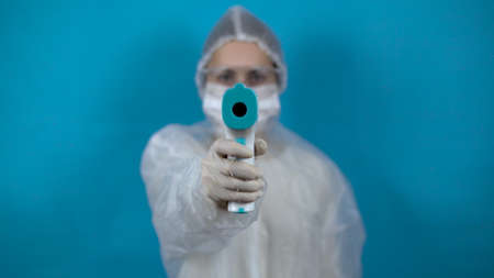 Young woman in a protective suit with an infrared thermometer. The girl measures the temperature...