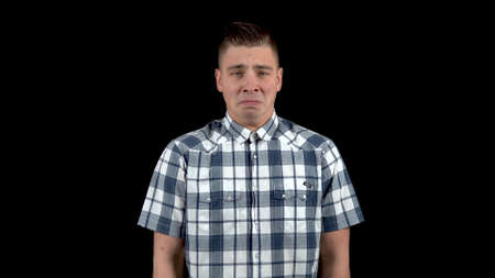 A young man shows an emotion of sadness. Sad man in a shirt on a black backgroundの写真素材