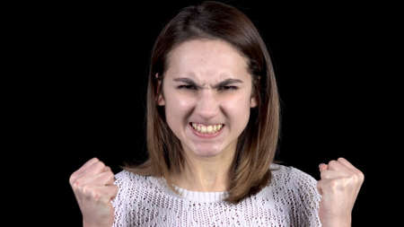 The young woman shows emotions of anger on his face. Girl grins teeth and frowns eyebrows on a black background closeup.の写真素材