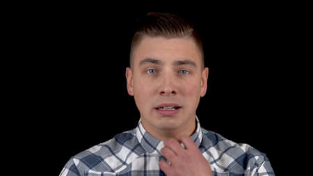 A young man shows an emotion of fear on his face. A person experiences fear. A man in a shirt on a black background closeupの写真素材