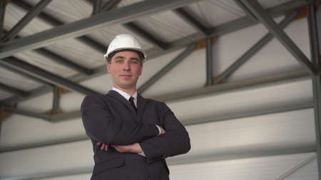 A young man in a protective helmet and shows a thumb at a construction site. The boss in a suit looks at the camera.の写真素材