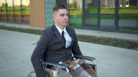 Young businessman in a suit in a wheelchair. A serious man is riding in a wheelchair against a...