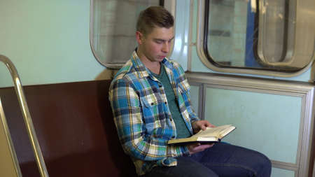 A young man reads a book in a subway train. Old subway carの写真素材