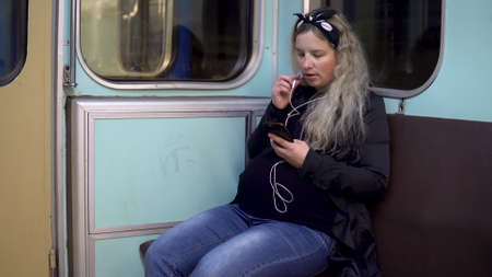 A pregnant woman is talking on the phone through headphones to a subway train. Old subway train carの写真素材