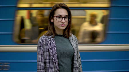 A young woman is standing in the subway. In the background a train ridesの写真素材