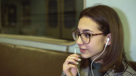 A young woman is talking on the phone through headphones in a subway train. Old subway carの写真素材