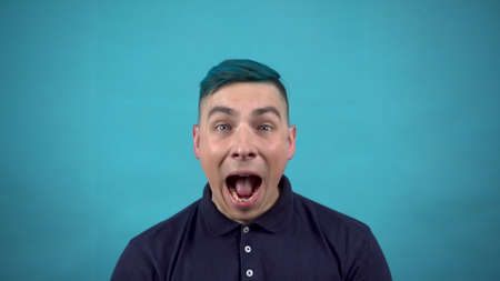 The young man in glasses with blue hair is surprised. Emotional man surprised on a blue background.の写真素材