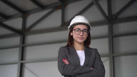 A young woman in a protective helmet crossed her arms and stands at a construction site. The boss woman in a suit looks at the camera.の写真素材