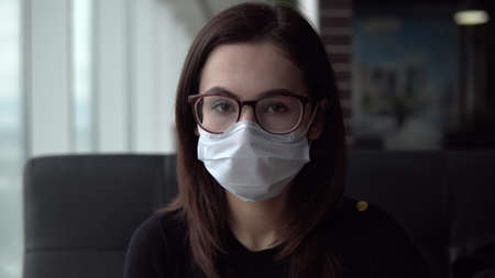 Young woman in a medical mask. A girl sits in a cafe by the window with a medical mask on her face. Prevention COVID-19.の写真素材