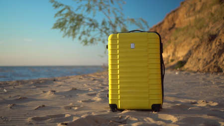 A yellow suitcase stands on the beach against the background of the sea. Travel suitcase.の写真素材
