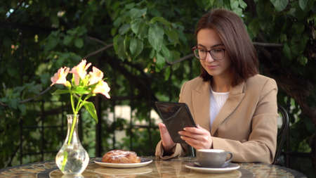 Young business woman sits in a cafe and writes text messages on a tablet.の写真素材