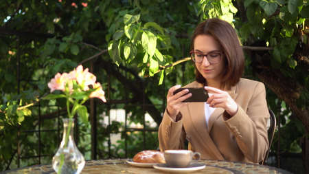 A young business woman sits in a cafe and photographs food on the phone.の写真素材