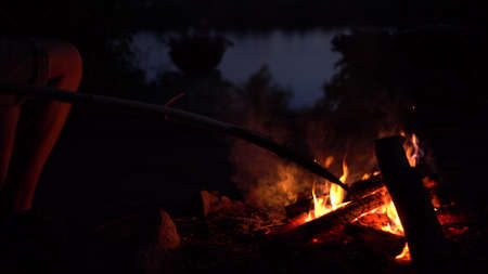 The man straightens the coals in the fire. The fire is burning in the middle of the night close-up.