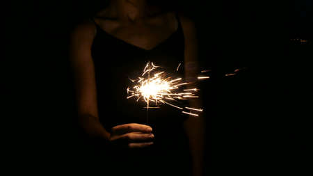 A woman holds a Bengal fire in her hand. Sparklers shine in the dark. Hand with a sparkler closeup