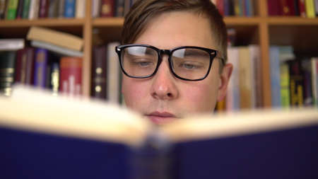 A young man is reading a book in a library. A man with glasses carefully looks at the book closeup....