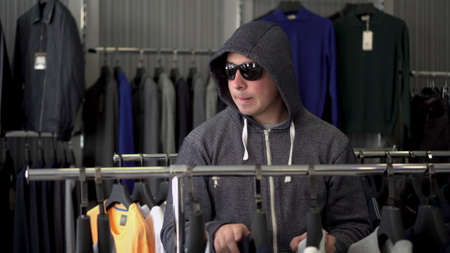 A man in a hood and glasses steals a T-shirt from a store. Clothing store.の写真素材