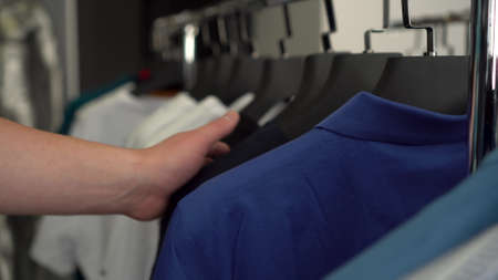A man runs his hand over T-shirts hanging on a hanger in a store close-up. Clothing store.の写真素材