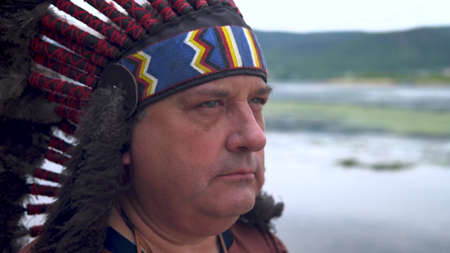 Old Native American Indian looks into the sunset. Background of the river. Close up.