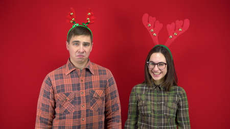 A young woman laughs at a young man because he has small horns, and the man is offended and cries red background.. People have worn headbands in the form of reindeer antlers.の写真素材