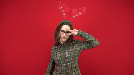 A young woman is dancing with a headband in the form of Christmas antlers. Studio shooting on a red background.の写真素材
