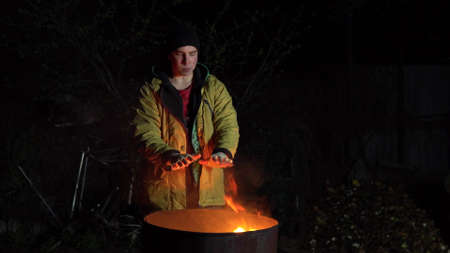 Homeless young man stands by the fire. A man stands at night near a barrel of fire and bask.の写真素材