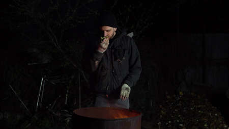 Homeless young man stands by the fire. A man stands at night near a barrel of fire and bask.の写真素材