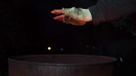 A homeless man warms his hands at night near a barrel of fire. Hands close up.の写真素材